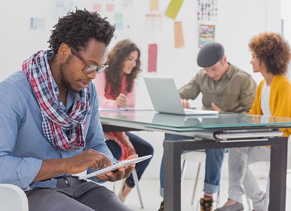 Four Designer On A Tablet And Laptop In A Meeting Space